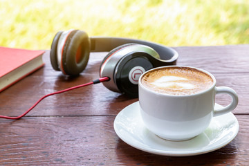 Cup of hot coffee and earphone on wooden
