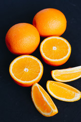Halves and slices of fresh juicy oranges on black textured background.