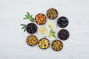 Fototapeta na wymiar Colorful olives and olive oil with olive leaves in a clay and white bowls on white wood plank background, top view.