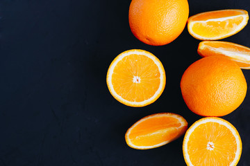 Halves and slices of fresh juicy oranges on black textured background with empty place for text.