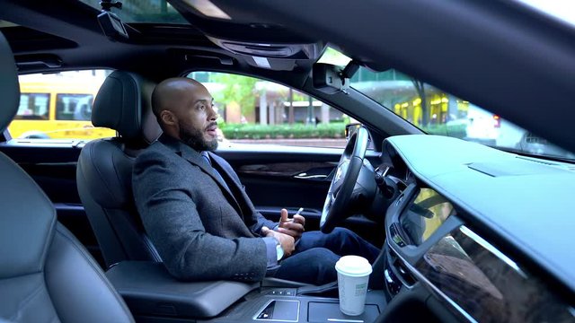 Executive businessman received phone call using bluetooth hands free speakerphone while sitting in car and using smartphone application, successful male trader with coffee to go talking at driver seat