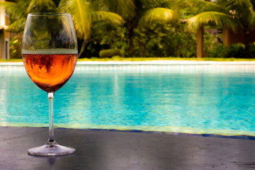 Crystal glass with fresh rosé wine next to a huge pool of crystal clear water. Luxury vacation concept.