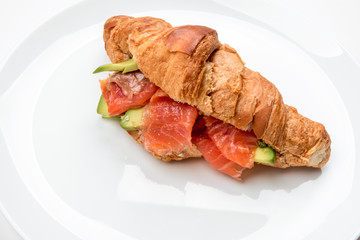 Croissant with salmon and avocado on a white plate.