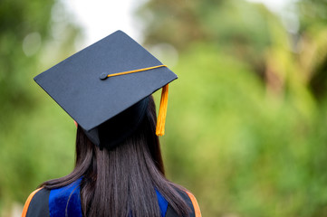 closeup behind a female college graduate wearing a black fringe gown and a black hat, Concept of...