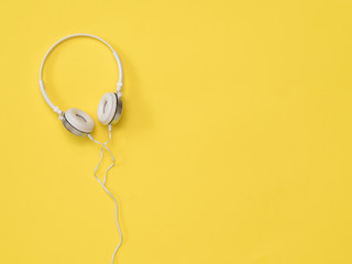 White headphones with a wire on a bright yellow background.