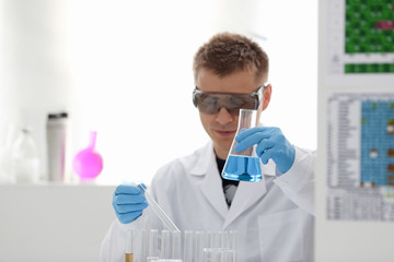 Male chemist holds test tube of glass in his hand overflows a liquid solution of potassium permanganate conducts an analysis reaction takes various versions of reagents using chemical manufacturing.