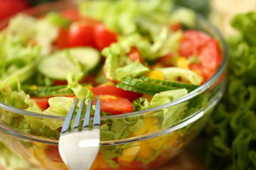 Silver fork in plate mixes salad fresh vegetables seasoned with olive oil. Raw food and vegetarian in modern society is popular concept.