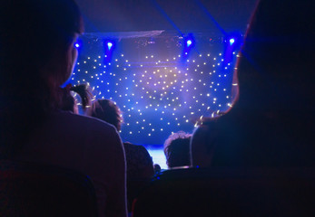 Blurred view of audience back. Silhouette shot from back in blue light. Multicolored light beams...