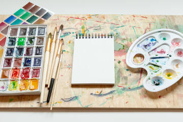 Set of watercolor paints, art brushes, palette and empty sketchbook. Art creativity concept.