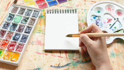 Artist painting with watercolor dye mockup flat lay. Top view on painter hand taking aquarelle paint in blank sketchbook. Art creativity concept.