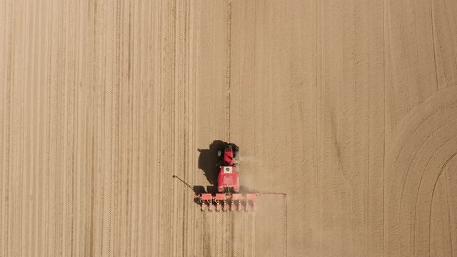 View from above, tractor working in a field. Tractor with a seeder, sow crops at field. Sowing agricultural crops. Tractor with a seeder to sowing in a huge field. Agricultural work. Spring sowing
