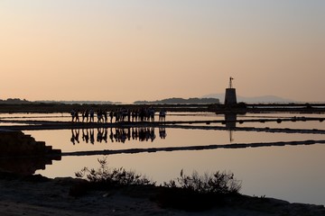 salt pans with water pumping tower and 
promontory in the background at sunset