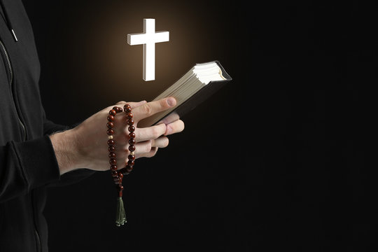 Religious young man praying to God on dark background