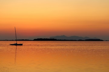 sailboat moored on the sea at sunset and headland on the background
