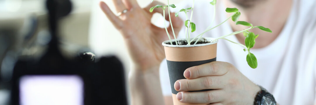 Male video blogger hold pot with green sprouts closeup background. Using camera and make selfie movie cincept