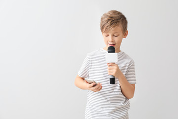 Little journalist with microphone and mobile phone on white background