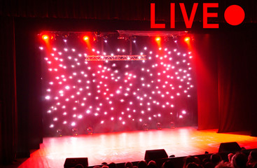 Text LIVE and red circle on blurred show background. Empty stage and sparkling stage lights at time of entertainment show. Concept live performance concert on the Internet, online show