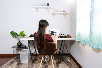 Fototapeta na wymiar Attractive young beautiful asian woman working with laptop and document while sitting at the indoors living room office as a freelancer, e-coaching working, remotely or work from home concept.