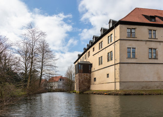 A moat in front of the historic Brake castle near the German city of Lemgo. It is winter with a blue sky and clouds. In the background a beautiful, old half-timbered house.