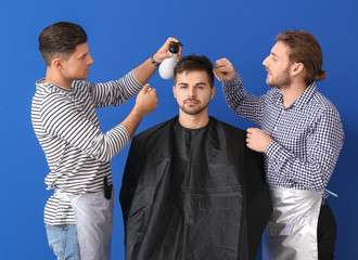 Young hairdressers working with client against color background