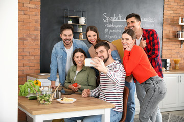 Young friends taking selfie while cooking together at home