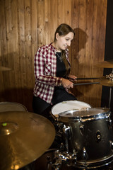 Professional drum set closeup. Beautiful young girl drummer in checkered shirt with drumsticks playing drums and cymbals, on the live country or rock music concert or in recording studio. Female drumm