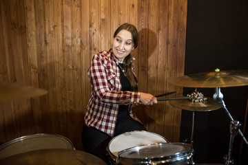 Professional drum set closeup. Beautiful young girl drummer in checkered shirt with drumsticks playing drums and cymbals, on the live country or rock music concert or in recording studio. Female drumm