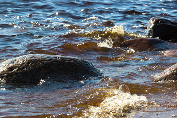 Sea background. Sea stones and surf, the wave hits the rocks. Sea water surface lit by sunny light. Summer sunny sea water scene. Nature concept. Beautiful summer landscape. Vacation concept.