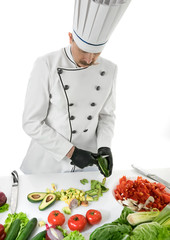 Chef cook peels the avocado with a knife at the white table with a vegetables