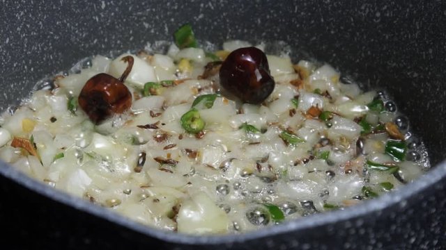 Frying Onions with green chilies, garlic, ginger and cumin seeds to make Tadka to make of spicy Indian lentils called Daal tadka. A 4K video resolution.