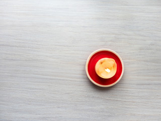 burning candle on a red stand on a light wooden background. View from above