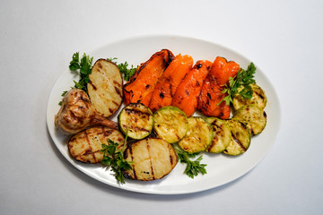 Grilled vegetables - pepper, zucchini, potato, garlic on a white plate