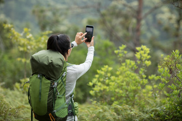 Woman hiker using smartphone taking pictures in spring mountain