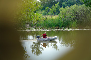 View of a man floating on a rubber inflatable boat with a motor through the leaves of trees