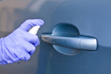 Man's hand in protective gloves cleaning car door handle using antibacterial or cleaning solution