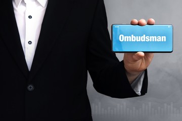 Ombudsman. Businessman in a suit holds a smartphone at the camera. The term Ombudsman is on the phone. Concept for business, finance, statistics, analysis, economy
