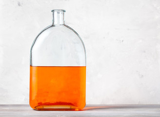 glass flask with orange watercolour solution on gray wooden board near gray concrete wall