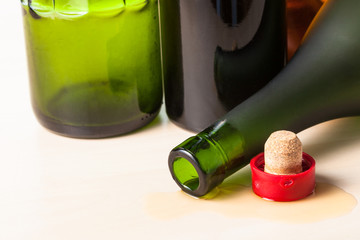 overturned brandy bottle and cork closeup near empty bottles on wooden board