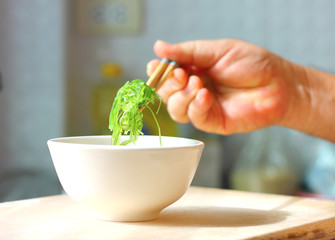 hand using bamboo chopsticks hold the seaweed over white bowl.