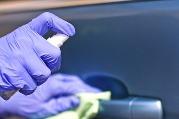 Man's hand in protective gloves cleaning car door handle using antibacterial or cleaning solution