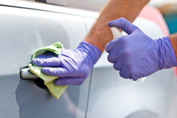 Men's hand in protective gloves cleaning car door handle using antibacterial or cleaning solution