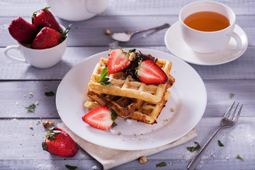 Plate of Belgian waffles with chocolate sauce and fresh  strawberries on white background. Delicious sweet dessert with cup of  tea.