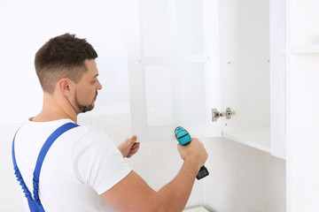 Worker installing kitchen furniture with electric screwdriver