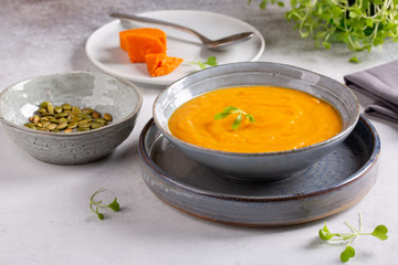 Vegetable cream soup in gray bowl on concrete background.  Sweet potato soup served with herbs and pumpkin seeds.