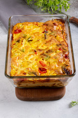 Vegetable clafoutis in glass baking dish on concrete background, savory pie with bell peppers, peas, onions and tomatoes.