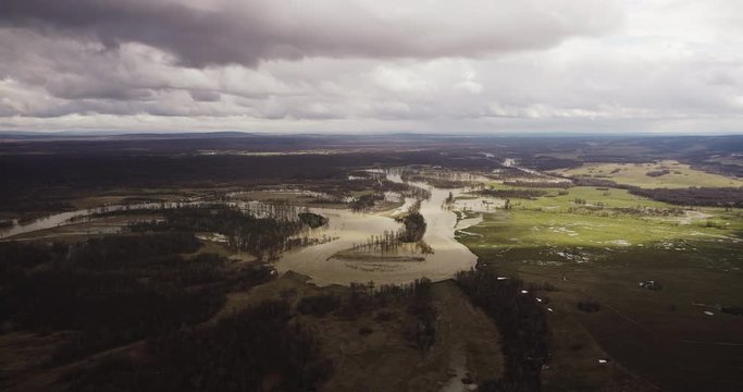 Flooded river floodplain with field and forest in wild lanscape. High altitude wide drone shot flooded area at spring time cloudy day