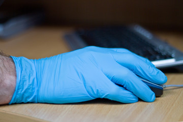 A hand in a rubber glove holds a computer mouse. Security concept for coronavirus, covid-19,