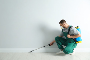 Pest control worker in uniform spraying pesticide indoors. Space for text