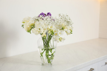 Beautiful bouquet with fresh freesia flowers in vase on cabinet indoors