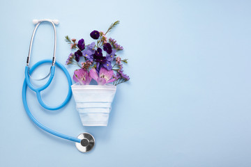 Flowers with mask and stethoscope on blue background. Happy nurse day concept. Top view